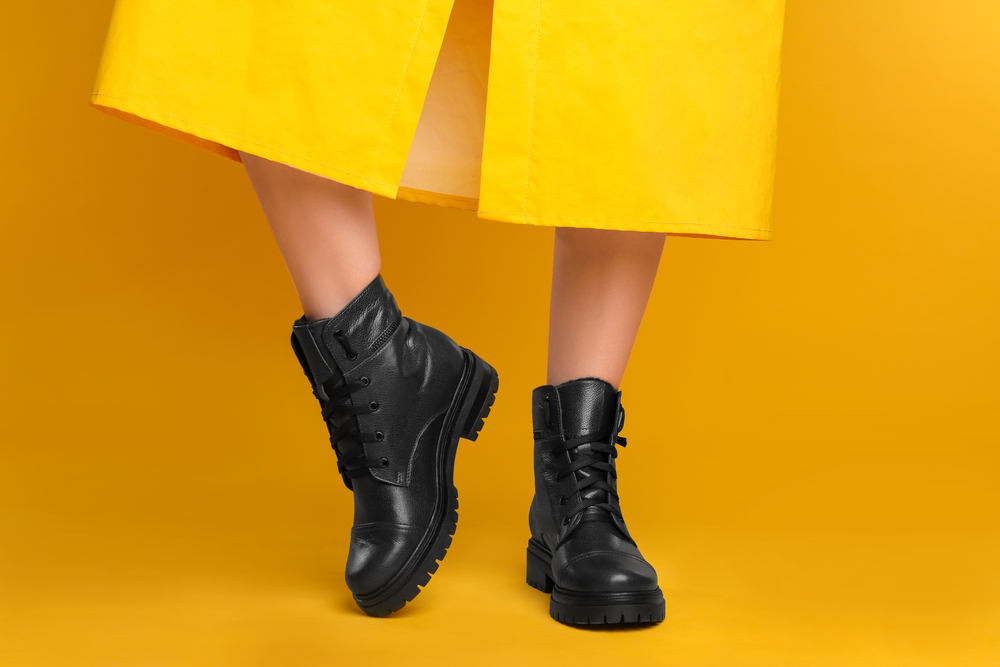 Woman wearing stylish boots on yellow background, closeup