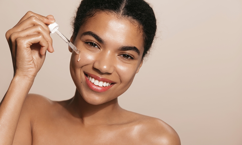 Smiling woman with perfect skin, applies face serum, holds dropper