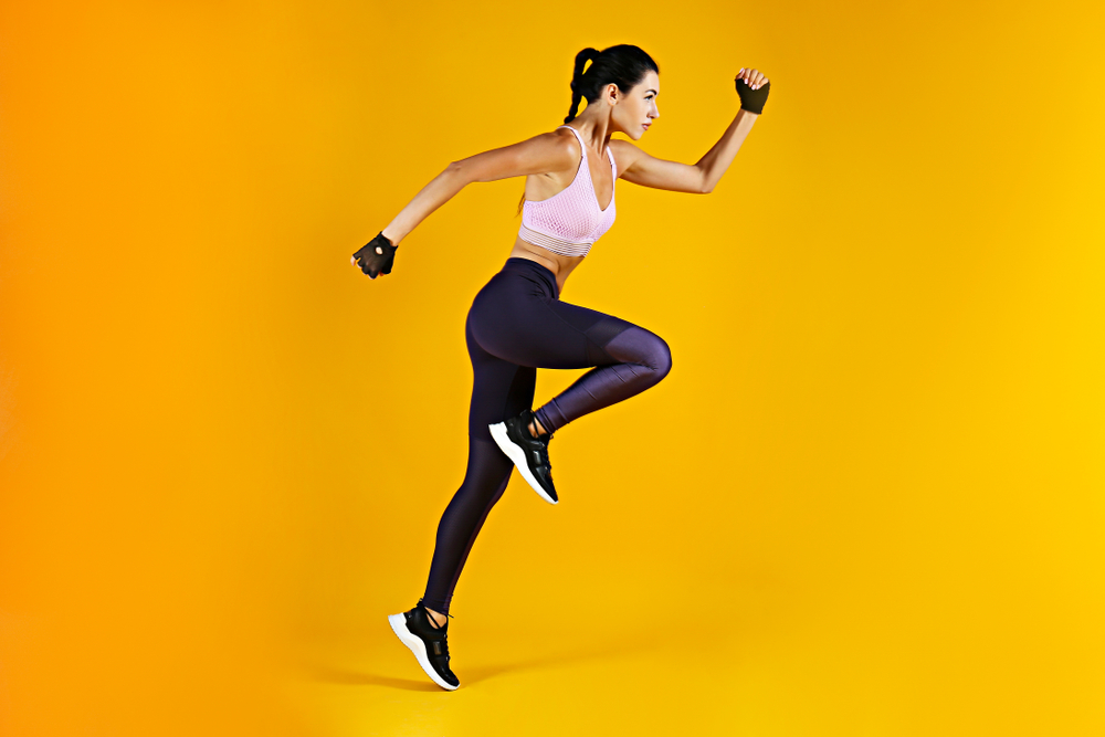 Close up shot of unrecognizable fit woman wearing blank tank top & yoga pants isolated on yellow background. Torso of slim attractive female with six pack belly in sportswear.