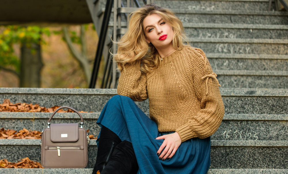 Fall fashion trend. Layer oversize knit over girly skirt. Wearable trends. Fall outfit formula. How to Style Sweater and Skirt Combo for Fall. Woman with gorgeous hairstyle sit on stairs outdoors.