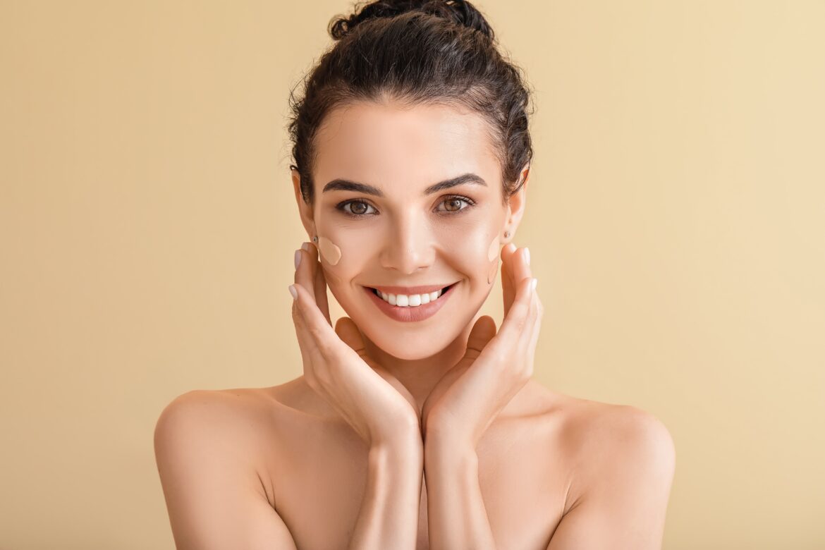 Beautiful young woman with foundation on her face against color background. considering concealer or foundation