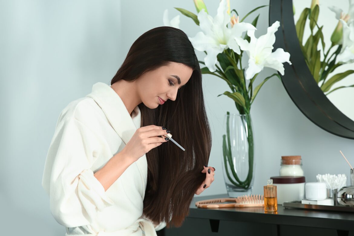 Beautiful young woman applying hair care products onto her healthy long hair for hair growth at home
