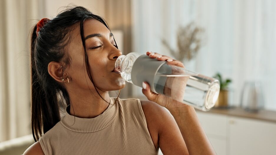 Drinking water, yoga or Indian woman in home with health, fitness or wellness for natural hydration. Thirsty female person, tired or healthy girl with liquid bottle after pilates to detox or relax
